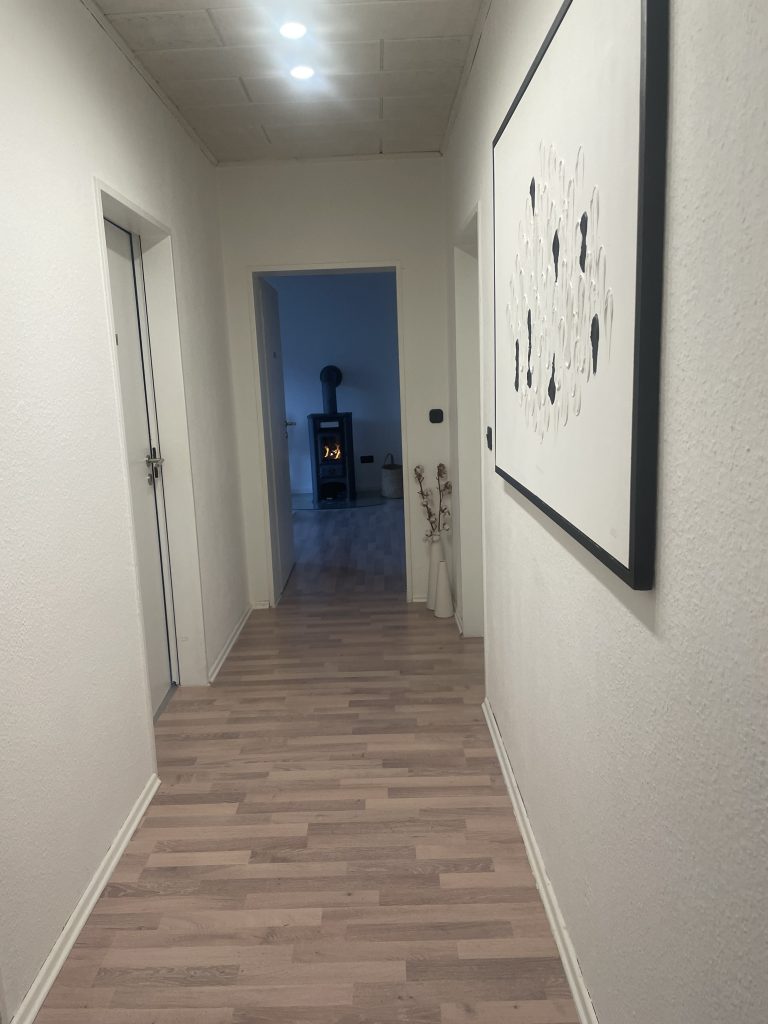 Ein Bild aus dem Flur, sobald man die Praxis betritt und etwas nach vorne geht. Geradeaus steht der Kaminofen